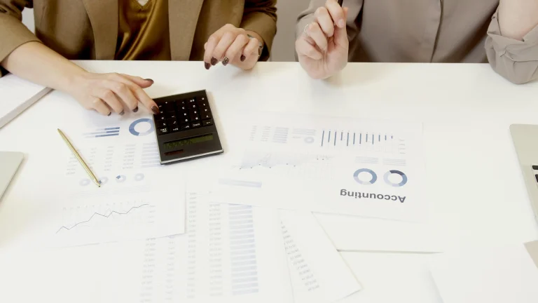 Two professionals analyzing accounting charts and data with a calculator on a desk – Accounting Course in Kerala. Accounting Course in Kerala