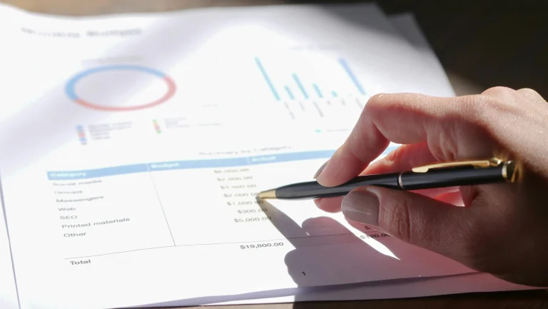 Close-up of a hand analyzing financial charts and budget reports with a pen – representing the CMA USA course focus on economic analysis. Best CMA USA Institute in Kerala – Enroll for Certified Management Accountant Training