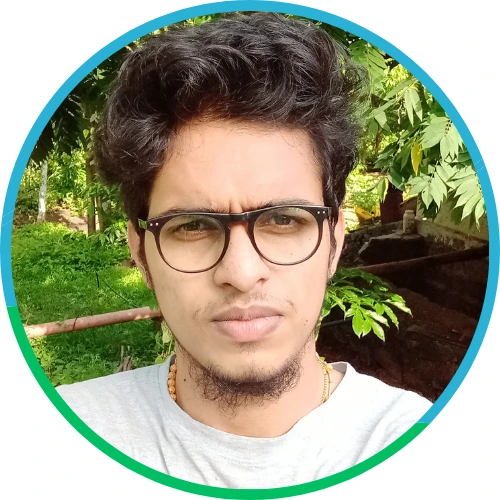 Portrait of a young man wearing glasses with curly hair and a short beard, taken outdoors with greenery in the background.